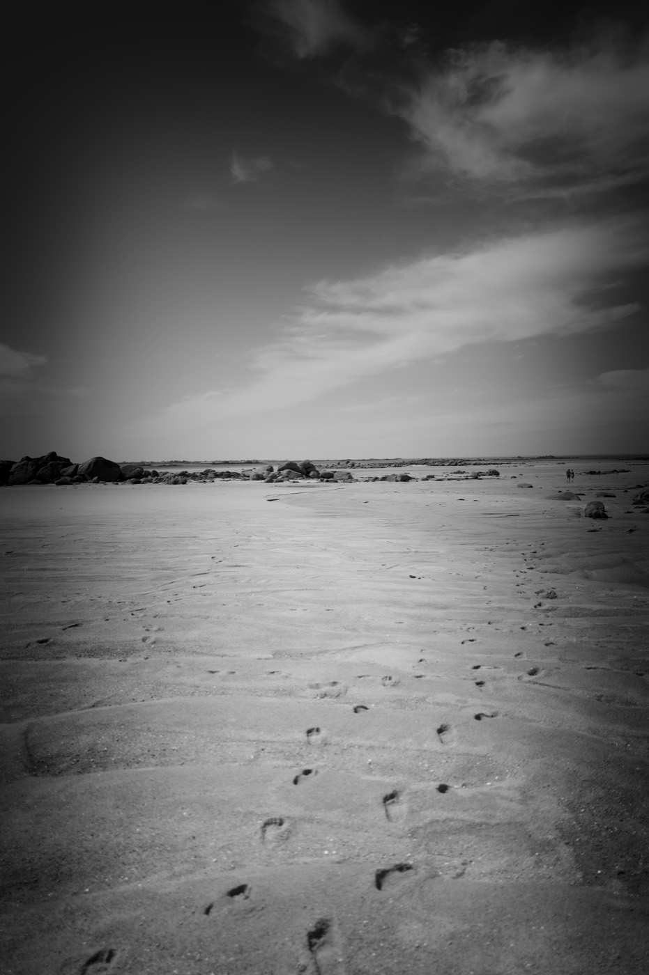 Des traces de pas sur le sable mouillé, la lumière rasante, le coin du cadre dans l'ombre.