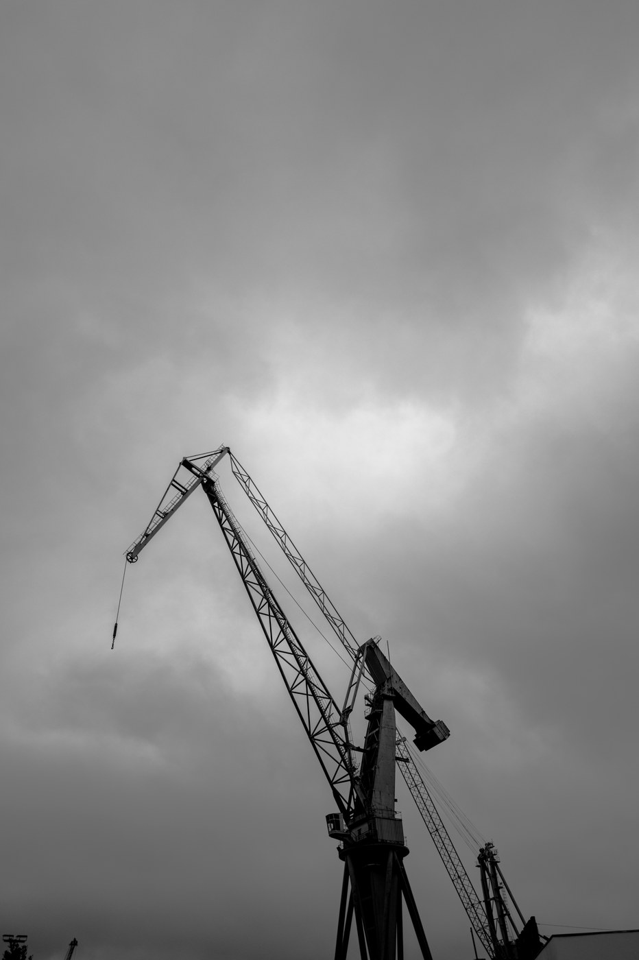 Une grue de chantier naval en silhouette, sa flèche penchée vers la gauche, sous un ciel de nuages lourds.