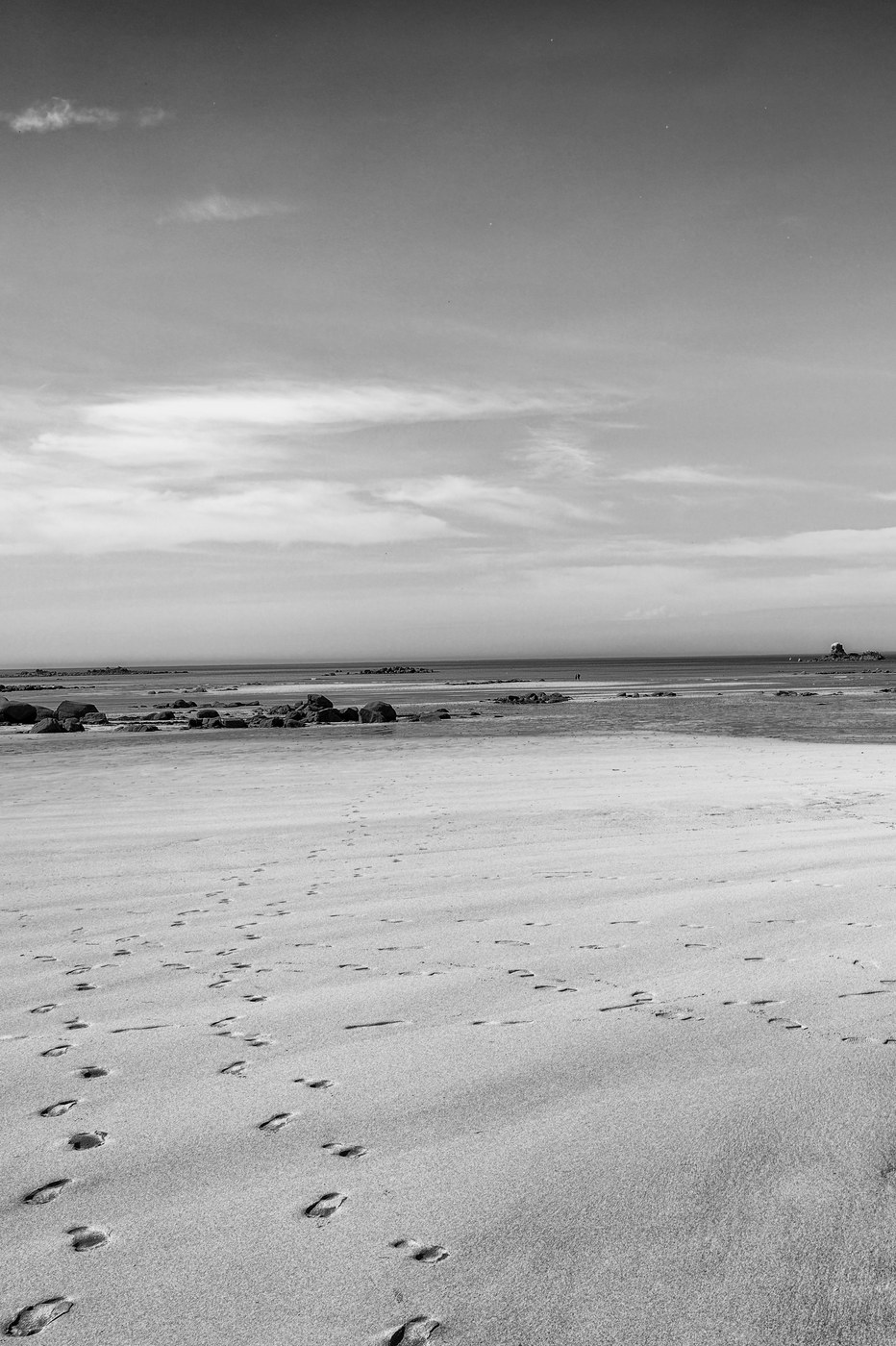Une ligne de pas s'éloigne en diagonale sur une plage vide, vers un horizon très bas ; le sable est clair et lisse.